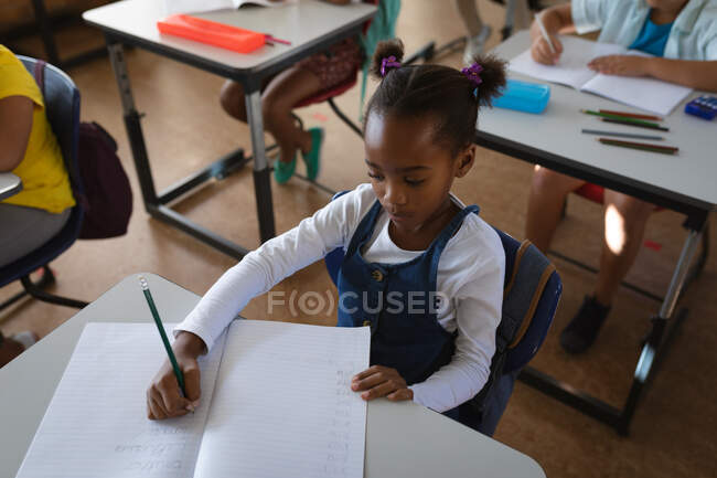 Afroamerikanerin lernt, während sie in der Schulklasse auf ihrem Schreibtisch sitzt. Schul- und Bildungskonzept — Stockfoto