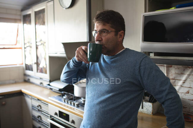 Homem caucasiano focado usando óculos, de pé na cozinha bebendo café. passar tempo livre em casa. — Fotografia de Stock