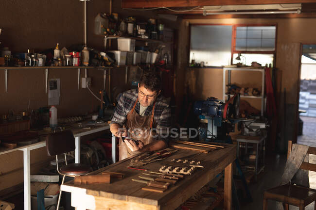 Кавказький чоловічий виробник ножів сидить за столом, використовуючи планшет у майстерні. Незалежний дрібний майстер на роботі.. — стокове фото