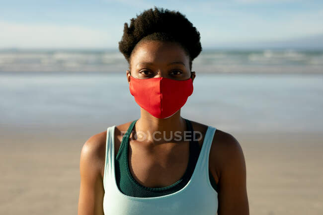 Portrait of african american woman wearing face mask practicing yoga,standing at the beach. healthy active lifestyle, outdoor fitness and well being during covid 19 pandemic. — Stock Photo