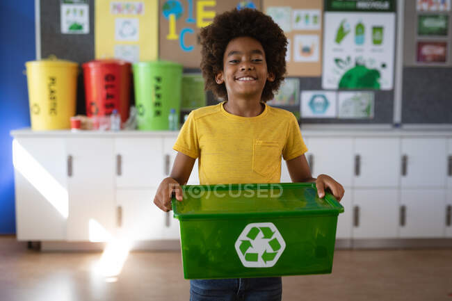 Retrato de menino afro-americano segurando bandeja cheia de itens de plástico reciclável na escola. conceito de escola e educação — Fotografia de Stock
