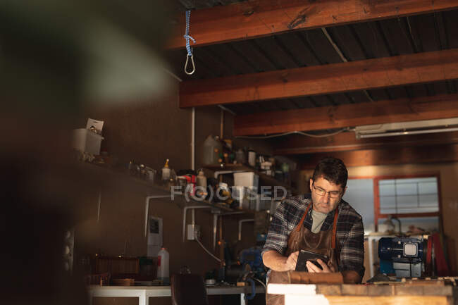 Couteau blanc homme fabricant assis au bureau, en utilisant la tablette en atelier. petit artisan indépendant au travail. — Photo de stock