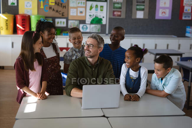 Kaukasische männliche Lehrer und eine Gruppe verschiedener Schüler lächeln, während sie in der Schule Laptop benutzen. Schul- und Bildungskonzept — Stockfoto
