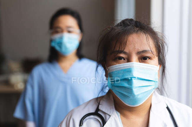 Retrato de dos médicas asiáticas con mascarillas en casa. atención médica y fisioterapia médica tratamiento. - foto de stock