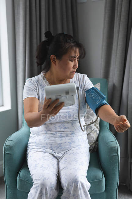 Asian woman sitting on couch and measuring pressure at home. healthcare and medical physiotherapy treatment. — Stock Photo