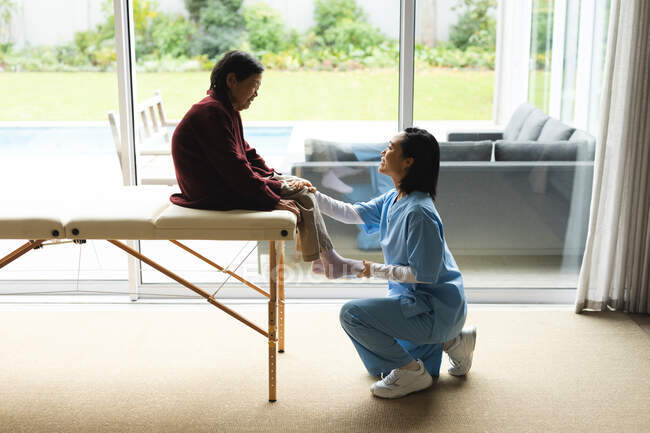 Physiothérapeute asiatique traitant une patiente âgée chez elle. soins de santé et physiothérapie médicale traitement. — Photo de stock