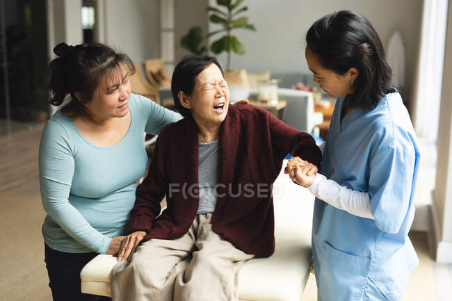 Fisioterapeuta asiática y su hija tratando a una paciente mayor en su casa. atención médica y fisioterapia médica tratamiento. - foto de stock