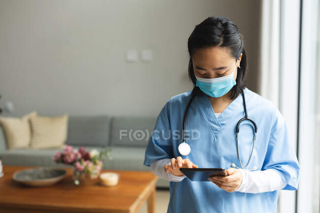 Fisioterapeuta asiática usando máscara facial e usando tablet em casa antes do tratamento. tratamento de saúde e fisioterapia médica. — Fotografia de Stock