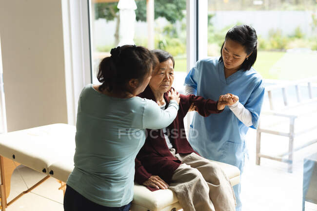 Asian female physiotherapist and daughter treating senior female patient at her home. healthcare and medical physiotherapy treatment. — Stock Photo