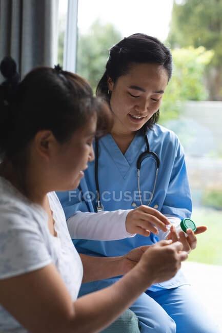 Азійська жінка-лікар дає коробку таблеток пацієнтки вдома. Медичне обслуговування та фізіотерапія. — стокове фото