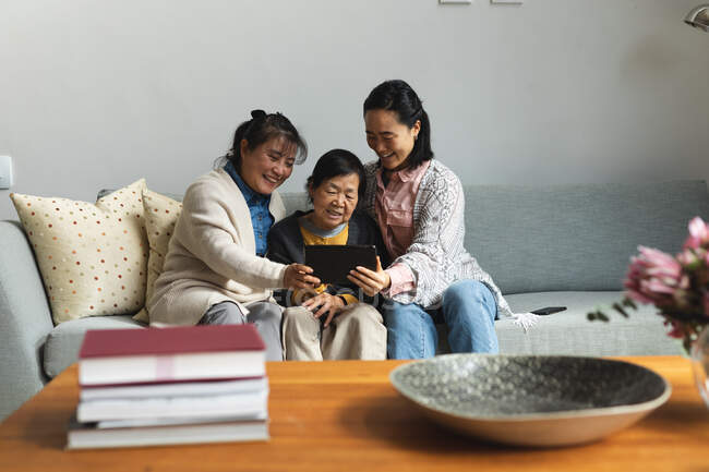 Glückliche ältere asiatische Frau zu Hause mit erwachsener Tochter und Enkelin mit Tablette. Seniorenleben, Zeit zu Hause mit der Familie verbringen. — Stockfoto