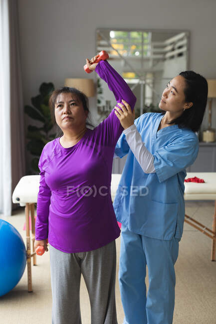 Fisioterapeuta asiática que trata a una paciente asiática en su casa. atención médica y fisioterapia médica tratamiento. - foto de stock