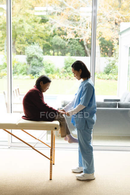 Asiatische Physiotherapeutin behandelt ältere Patientinnen zu Hause. Gesundheitswesen und medizinische physiotherapeutische Behandlung. — Stockfoto