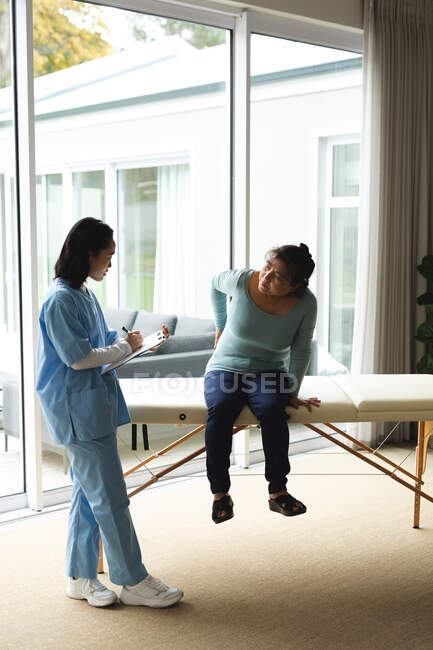 Fisioterapeuta asiática que trata a una paciente mayor en su casa. atención médica y fisioterapia médica tratamiento. - foto de stock