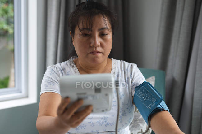 Mujer asiática sentada en el sofá y midiendo la presión en casa. atención médica y fisioterapia médica tratamiento. - foto de stock