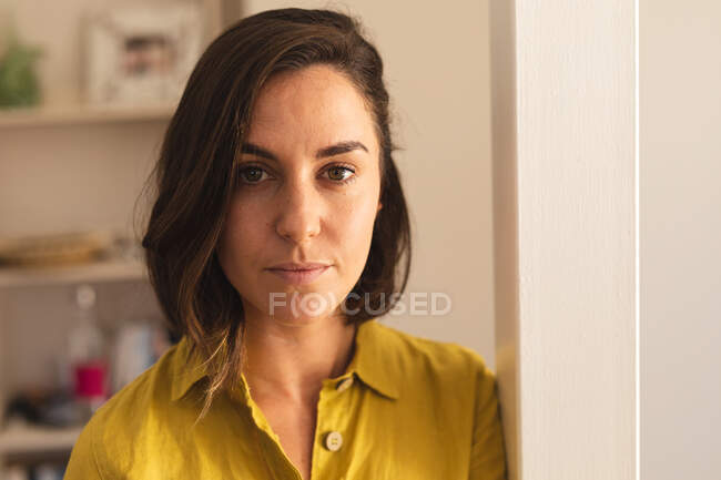 Retrato de mujer caucásica vistiendo camisa amarilla y mirando a la cámara. estilo de vida doméstico, pasar tiempo libre en casa. - foto de stock