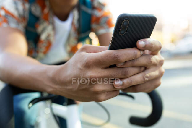 African american man in city sitting on bike and using smartphone. digital nomad on the go, out and about in the city. — Stock Photo