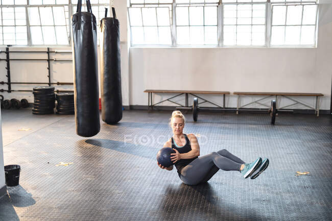 Mulher caucasiana forte se exercitando no ginásio, fazendo sit-ups usando bola. treinamento cruzado de força e aptidão para boxe. — Fotografia de Stock
