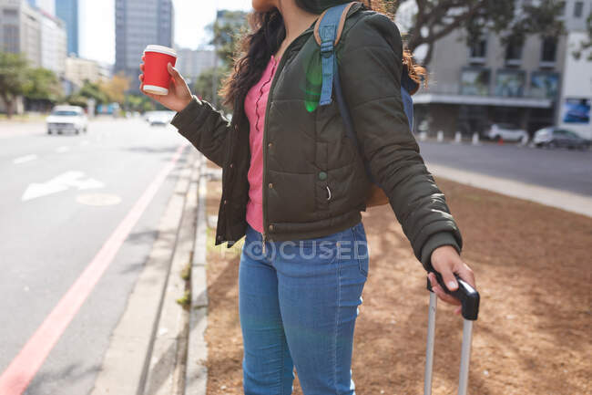 Frau am Straßenrand mit Koffer und Kaffee zum Mitnehmen. Unabhängige junge Frau in der Stadt unterwegs. — Stockfoto