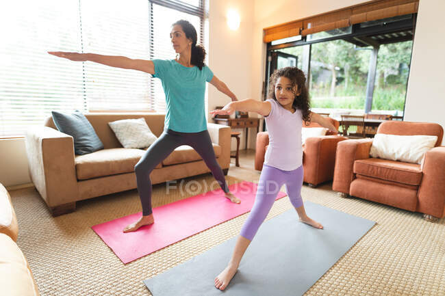 Mixed race mother and daughter practicing yoga in living room. domestic lifestyle and spending quality time at home. — Stock Photo