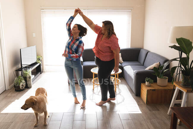 Glückliches lesbisches Paar tanzt und lächelt im Wohnzimmer. häuslicher Lebensstil, Freizeit zu Hause verbringen. — Stockfoto