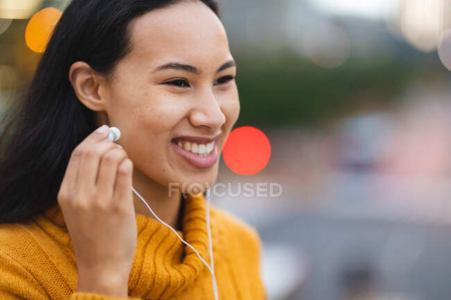 Mujer asiática sonriente con auriculares en la calle. mujer joven independiente fuera y alrededor de la ciudad. - foto de stock