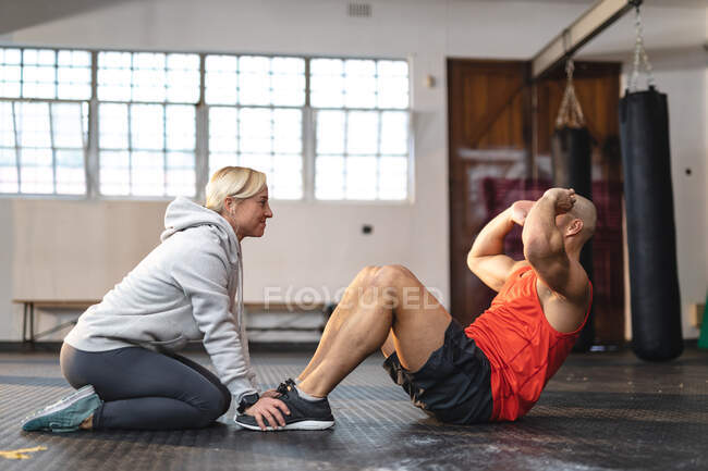 Caucasiano treinador do sexo feminino instruindo homem se exercitando no ginásio, fazendo sit ups. treinamento cruzado de força e aptidão para boxe. — Fotografia de Stock