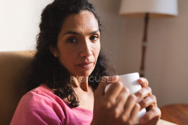 Retrato de mulher de raça mista sentado no sofá e beber café. estilo de vida doméstico e passar tempo de qualidade em casa. — Fotografia de Stock