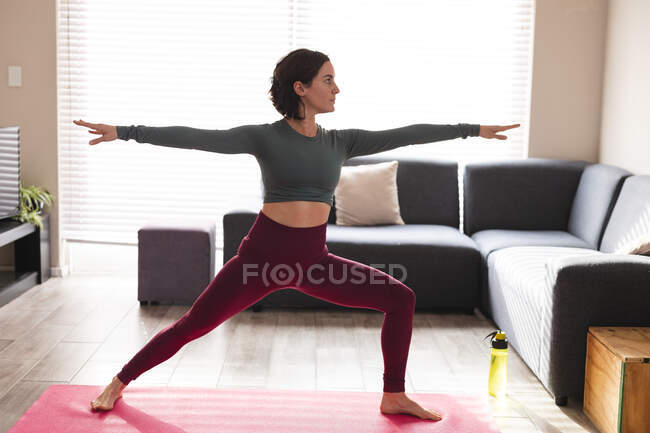 Femme caucasienne pratiquant le yoga, s'étirant sur un tapis de yoga. mode de vie domestique, passer du temps libre à la maison. — Photo de stock