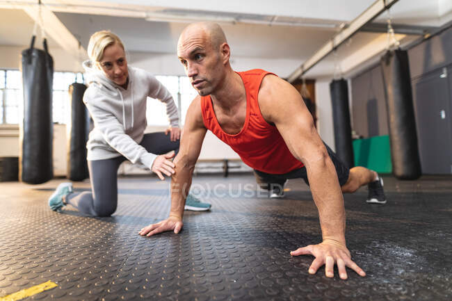 Кавказская женщина-тренер инструктирует мужчину тренировками в спортзале, делает отжимания. силовые и фитнес-кросс тренировки для бокса. — стоковое фото