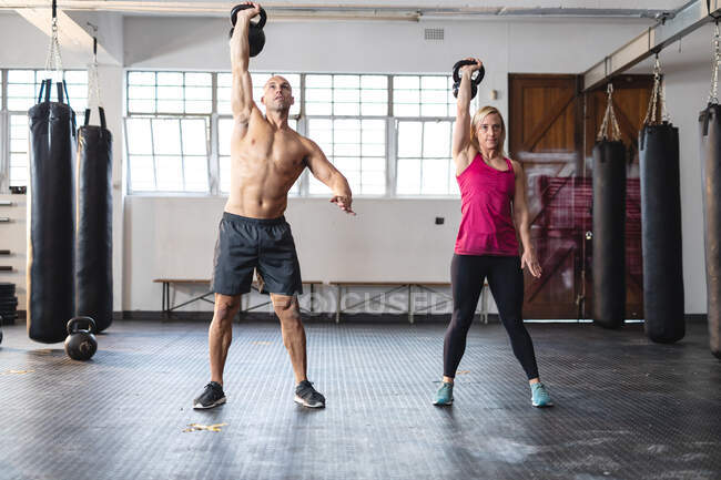 Homem e mulher caucasianos fortes se exercitando no ginásio, levantando pesos. treinamento cruzado de força e aptidão para boxe. — Fotografia de Stock