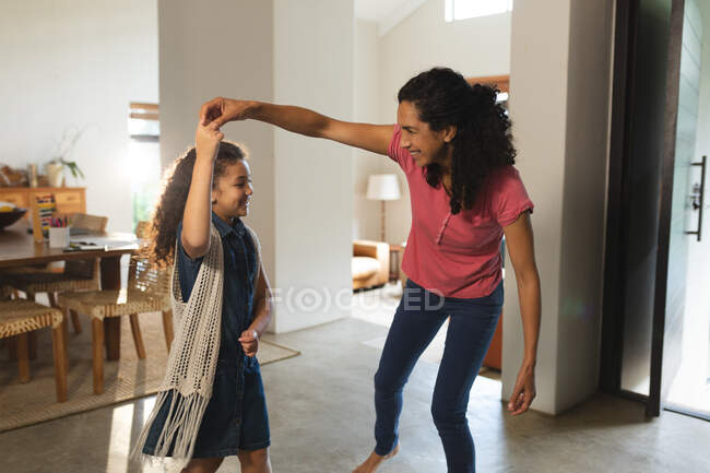 Happy mixed race mother and daughter dancing in living room. domestic lifestyle and spending quality time at home. — Stock Photo