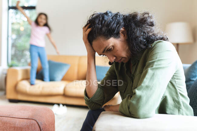 Tired mixed race mother sitting on sofa, having headache. domestic lifestyle and spending quality time at home. — Stock Photo