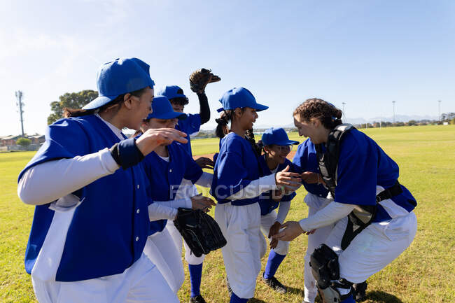 Diverse group of happy female baseball players celebrating on sunny baseball field after game. female baseball team, sports training, togetherness and commitment. — Stock Photo