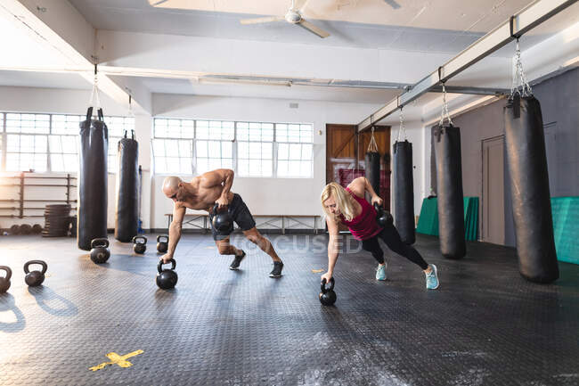 Hombre y mujer caucásicos haciendo ejercicio en el gimnasio, haciendo flexiones con pesas. entrenamiento cruzado de fuerza y fitness para boxeo. - foto de stock