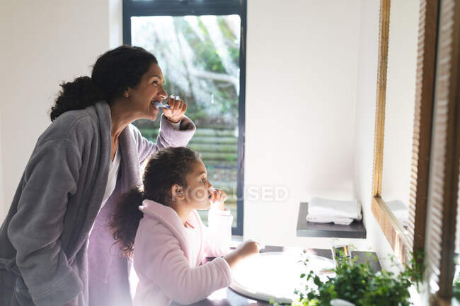 Midsection of mixed race mother and daughter brushing teeth in bathroom. domestic lifestyle and spending quality time at home. — Stock Photo