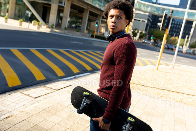 Un Afro-Américain en ville tenant du skateboard. nomade numérique en déplacement, en déplacement dans la ville. — Photo de stock