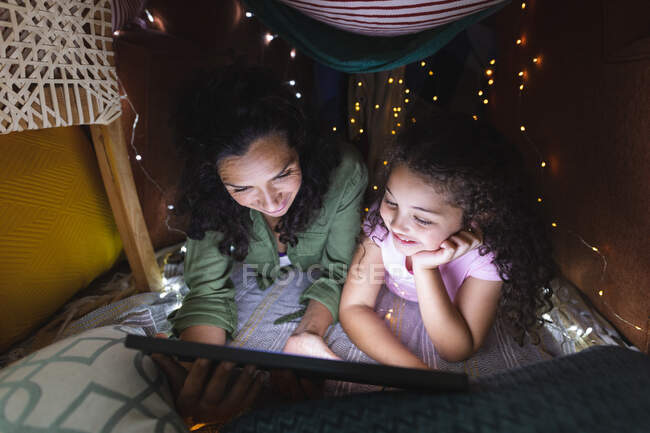Happy mixed race mother and daughter using laptop in makeshift tent. domestic lifestyle and spending quality time at home. — Stock Photo