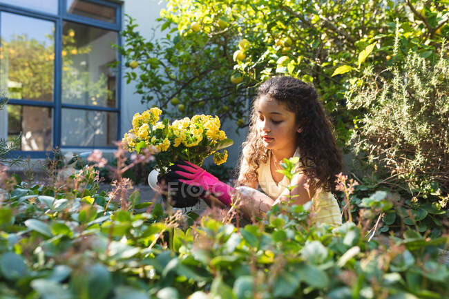 Sonriente chica de raza mixta plantando flores en el patio trasero. estilo de vida doméstico y pasar tiempo de calidad en casa. - foto de stock