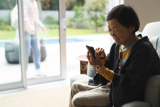 Feliz mulher asiática sênior em casa usando smartphone. estilo de vida sênior, tecnologia, passar tempo em casa. — Fotografia de Stock