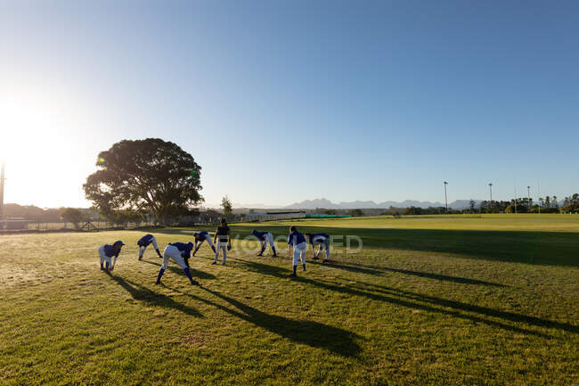 Diverso grupo de jugadoras de béisbol con entrenador calentándose en el campo soleado, estirándose. equipo femenino de béisbol, entrenamiento deportivo, unión y compromiso. - foto de stock