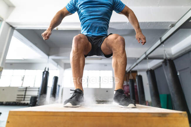 Hombre caucásico haciendo ejercicio en el gimnasio, saltando en la caja. entrenamiento cruzado de fuerza y fitness para boxeo. - foto de stock
