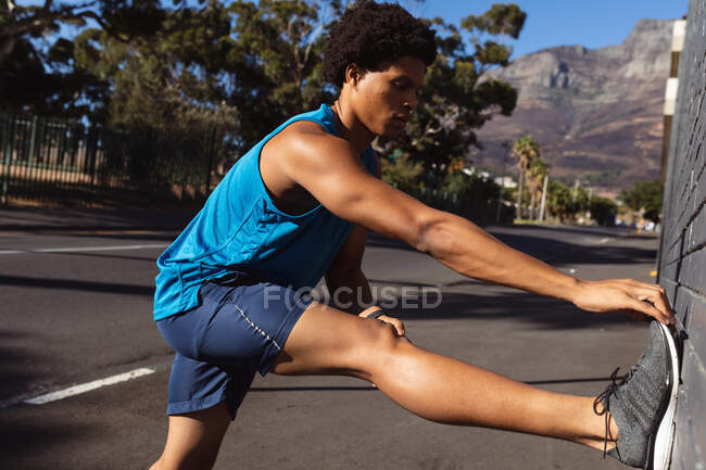 Ajuste hombre afroamericano haciendo ejercicio en la ciudad que se extiende en la calle. fitness y estilo de vida urbano activo al aire libre. - foto de stock