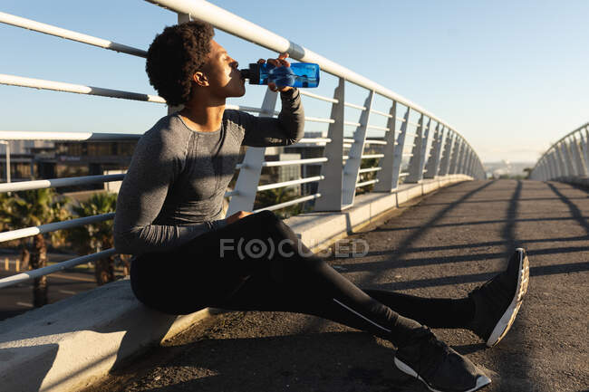 Fit african american man exercising in city resting and drinking water. fitness and active urban outdoor lifestyle. — Stock Photo