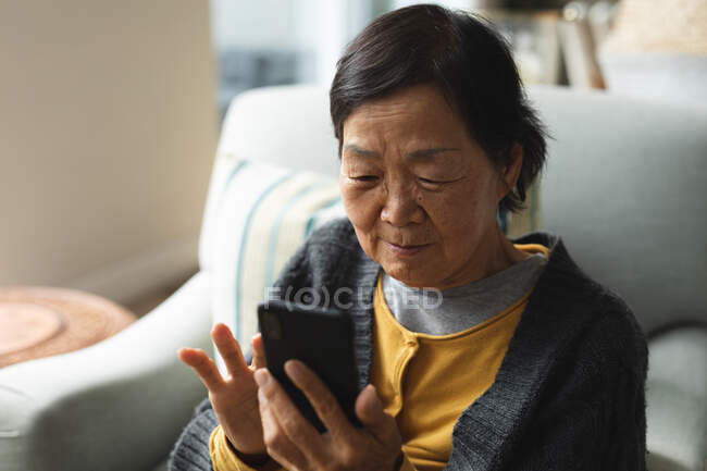 Feliz mujer asiática senior en casa usando smartphone. estilo de vida senior, tecnología, pasar tiempo en casa. - foto de stock