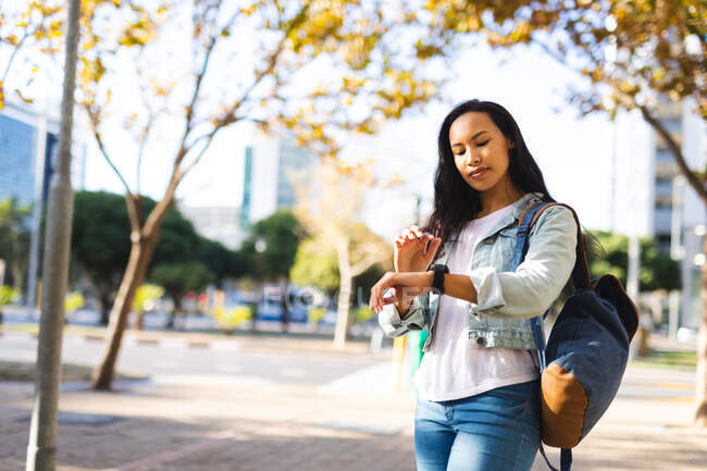 Asiatin checkt im sonnigen Park ihre Smartwatch. Unabhängige junge Frau in der Stadt unterwegs. — Stockfoto
