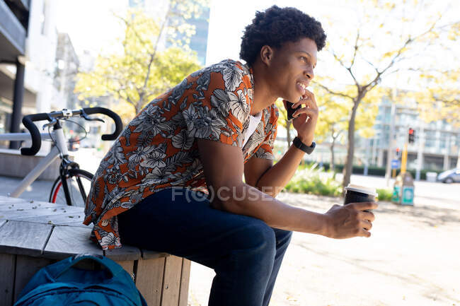 Homem afro-americano na cidade sentado e usando smartphone. nômade digital em movimento, para fora e sobre na cidade. — Fotografia de Stock