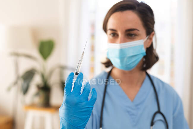 Caucasian female doctor wearing face mask preparing vaccine. medical and healthcare services during coronavirus covid 19 pandemic. — Stock Photo