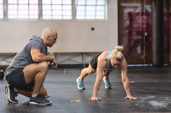 Entrenador masculino caucásico instruyendo a la mujer haciendo ejercicio en el gimnasio, haciendo flexiones de presión. entrenamiento cruzado de fuerza y fitness para boxeo. - foto de stock