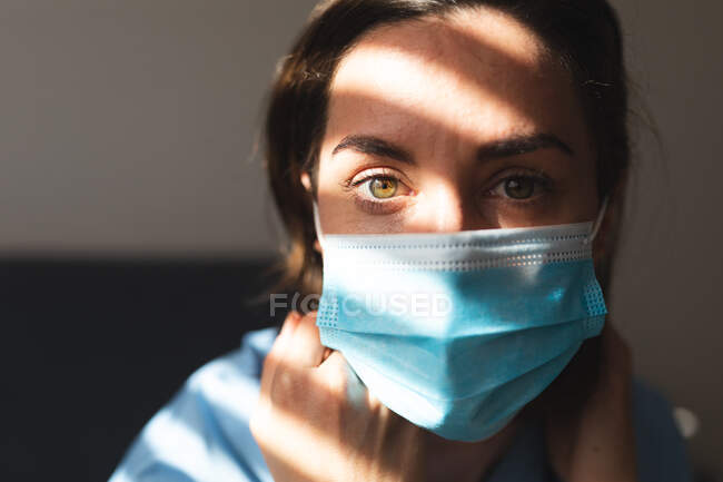 Retrato de médica caucasiana vestindo máscara facial e olhando para a câmera. serviços médicos e de saúde durante a pandemia do coronavírus covid 19. — Fotografia de Stock